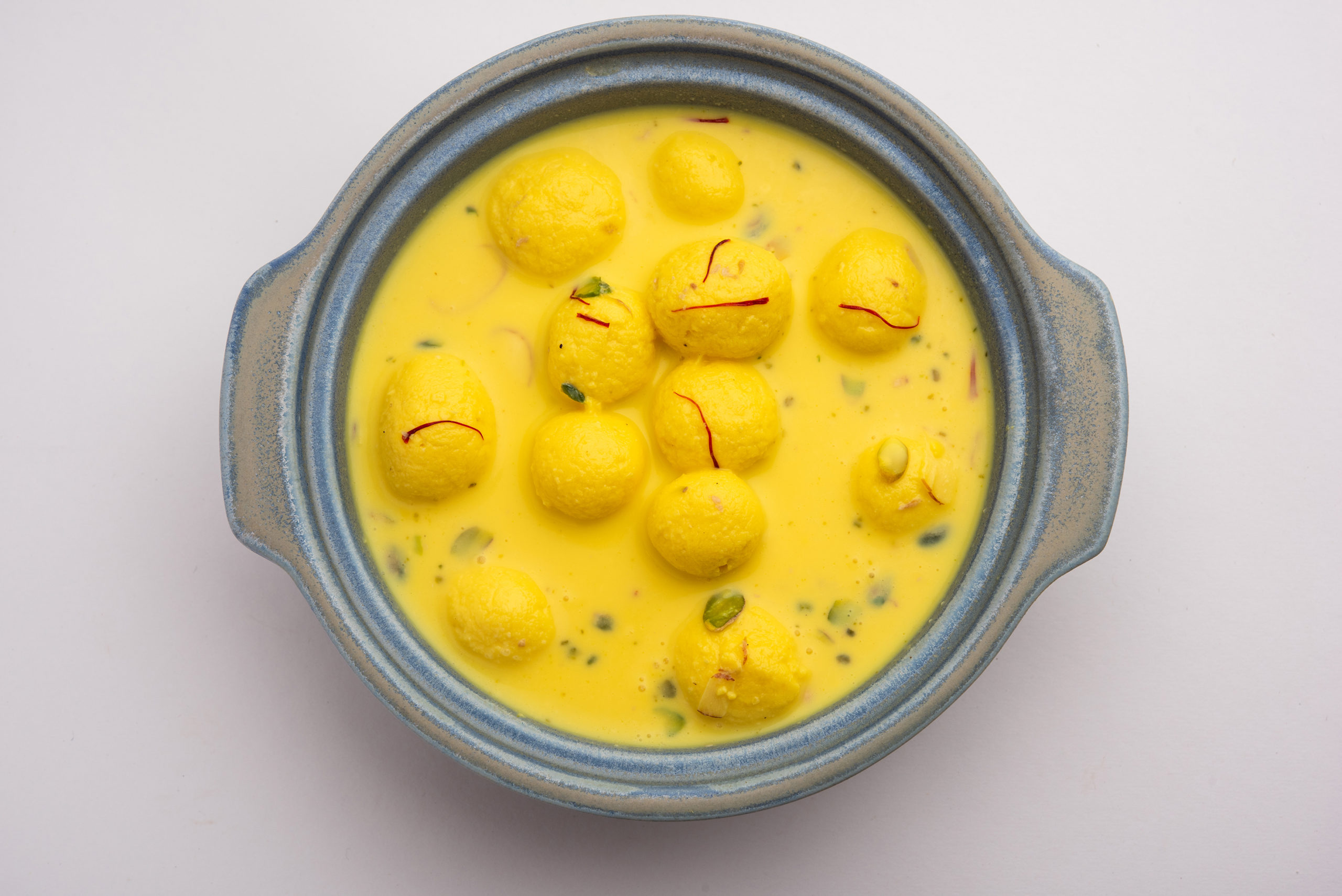 Angoori Rasmalai is an Indian dessert sweet with dry fruits and Saffron toppings, served in a bowl over moody background. selective focus